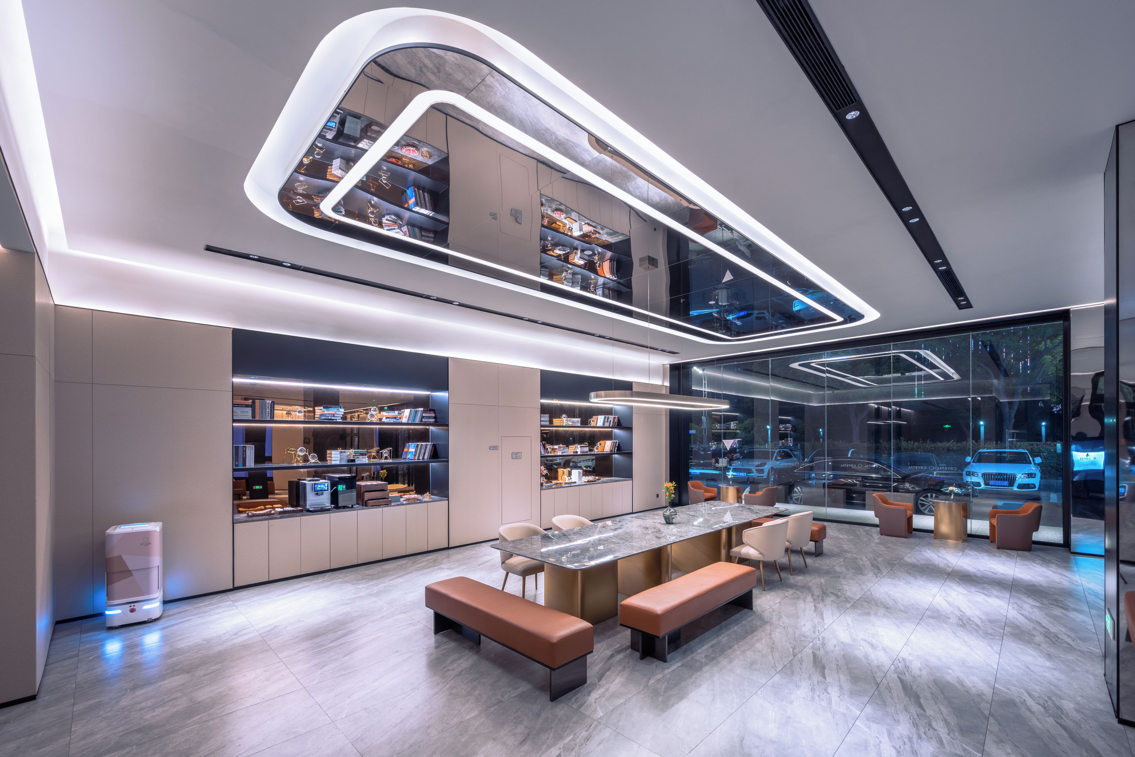 Un hall d’hôtel moderne doté d’un espace salon central, d’un grand écran numérique et d’un mur de verre donnant sur la rue.