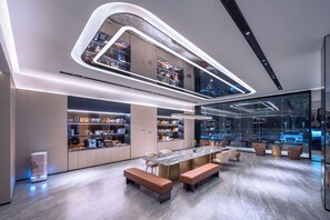 Un hall d’hôtel moderne doté d’un espace salon central, d’un grand écran numérique et d’un mur de verre donnant sur la rue.