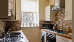 A compact kitchen with a window, a stove, oven, and a microwave. - Puffin View - One Bedroom Cottage, Sleeps 2 (Llanfairfechan)
