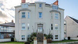 A multi-story residential building with a symmetrical facade, multiple windows, and a central entrance with a staircase. - Puffin View - One Bedroom Cottage, Sleeps 2 (Llanfairfechan)