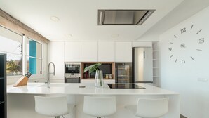 Una cocina moderna con armarios blancos, una isla central con taburetes y una estufa integrada, además de un refrigerador de acero inoxidable.