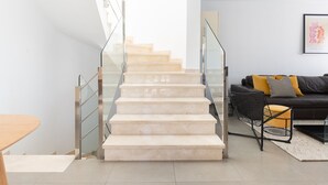 Un interior moderno con una escalera, un sofá negro con cojines amarillos y una obra de arte enmarcada en la pared.