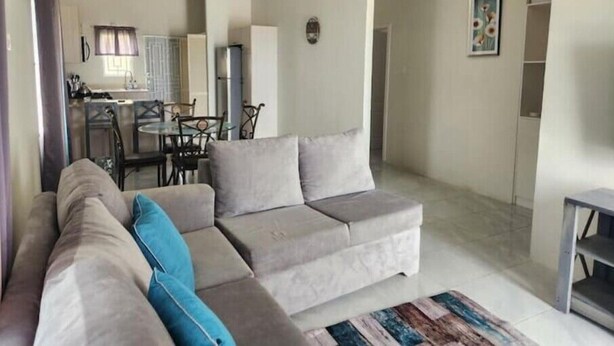 Uma sala de estar com sofá, um espaço de jantar com cadeiras e mesa, e uma cozinha ao fundo.