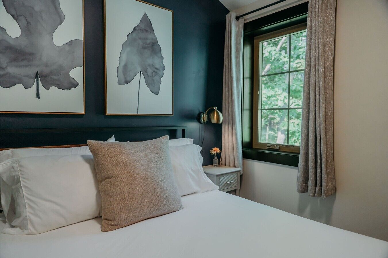 A bedroom with a bed, pillows, a nightstand, a lamp, and artwork on the wall.
