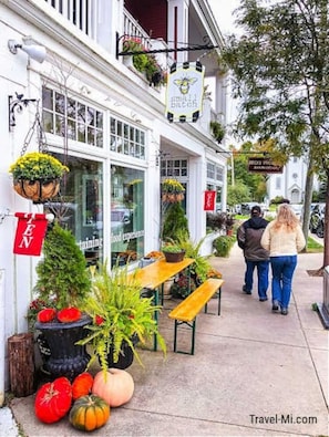 A storefront with hanging flower baskets, a bench, and potted plants outside.