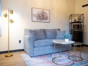 A modern living room with a grey sofa, a small round table, a floor lamp, and a framed artwork on the wall.