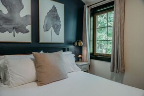 A bedroom with a bed, pillows, a nightstand, a lamp, and artwork on the wall.