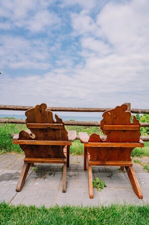 Dos sillas Adirondack de madera mirando un cuerpo de agua, con una zona de césped y una valla de madera al fondo.
