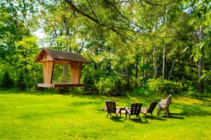 Uma casa de pássaros de madeira pendurada em uma árvore em um jardim verdejante, com cadeiras e uma mesa.
