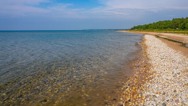 Ein Blick auf einen Kiesstrand mit ruhigem Wasser und einer fernen Küste.