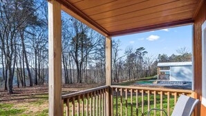 Une terrasse en bois avec une chaise, donnant sur une zone boisée et un petit bâtiment.
