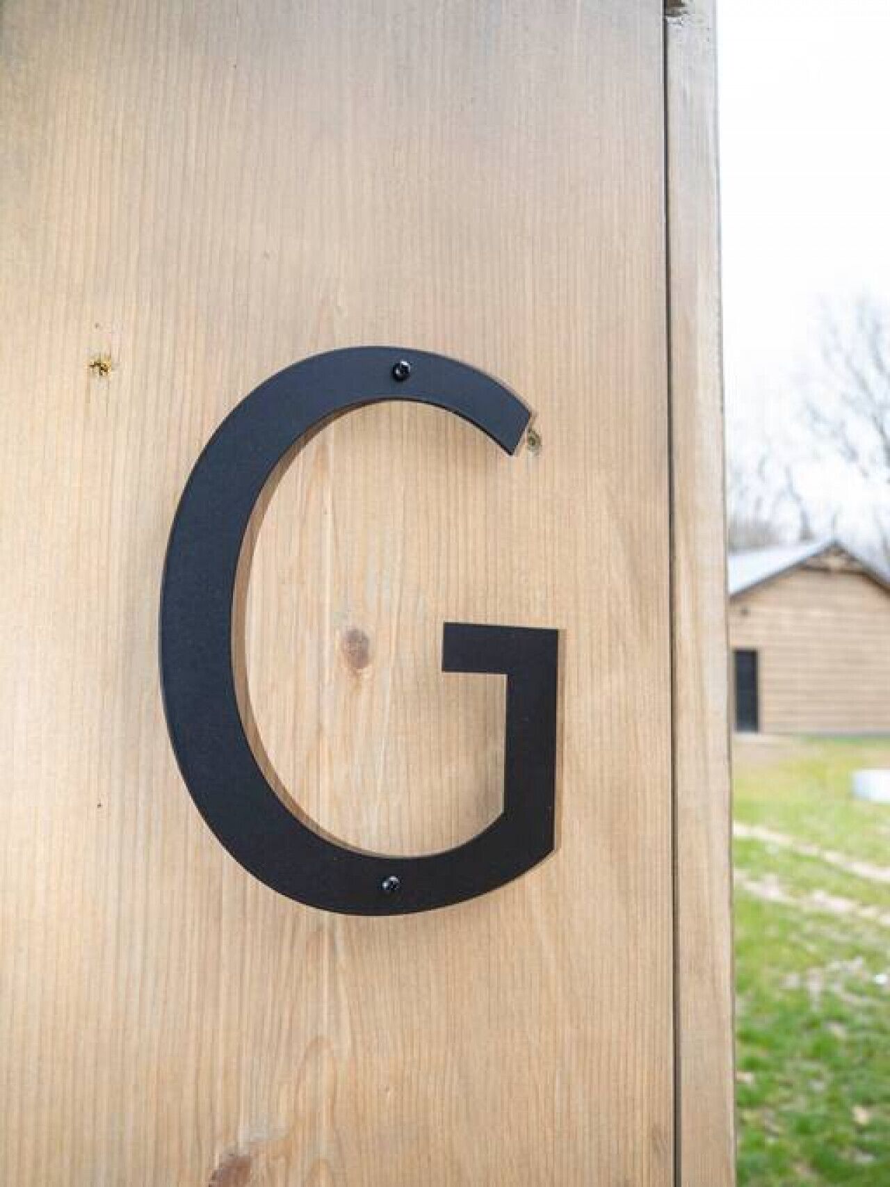 Une porte en bois sur laquelle est fixée une lettre « G » noire.