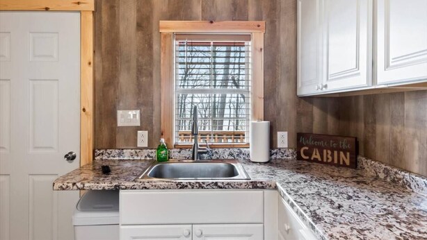 A kitchen with wooden walls, a granite countertop, a sink, and a window with blinds. - Tiny cabin on 10 acres with pond (Albertville)