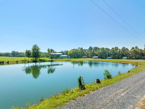 A tranquil lakeside scene with a gravel path, a small pond, and several buildings in the background.