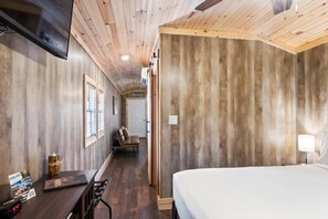 A hotel room with a wooden ceiling, a bed, a desk with a computer, a chair, and a TV mounted on the wall.