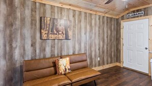 A room with a wooden wall, a brown leather sofa with a deer print pillow, a ceiling fan, and a door labeled "ALABAMA".