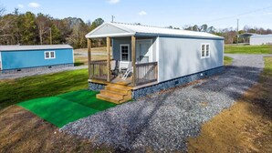 A small, single-story mobile home with a porch and a green carpeted area in front.
