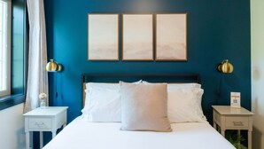 A hotel room with a large bed, two bedside tables, a nightstand, a window with curtains, and three framed pictures on the wall.