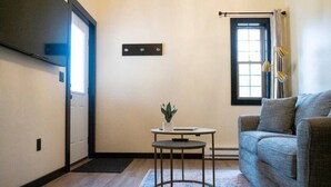 A living room with a sofa, a small round table with a plant, a window with curtains, and a door.