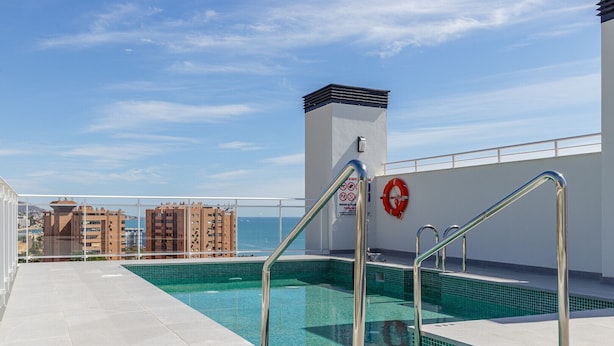 A rooftop pool with clear blue water, metal railings, and a lifebuoy on the wall.