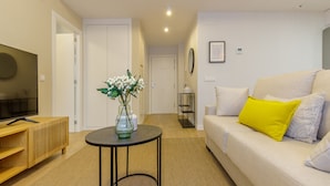 A modern living room with a sofa, a TV, a small table with a vase, and a hallway leading to a door.