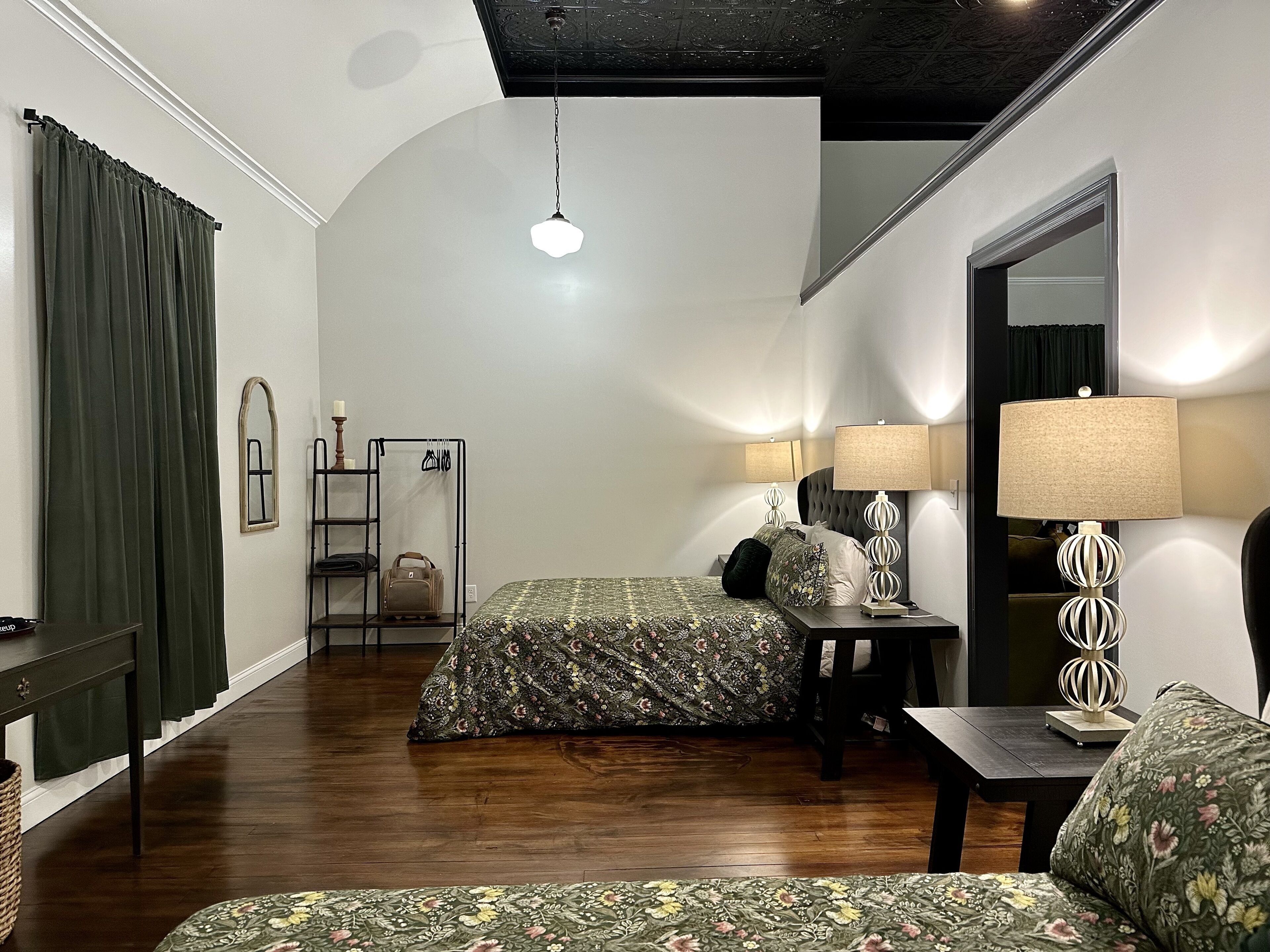 A bedroom with two beds, a nightstand, a mirror, a hanging light fixture, and a wooden floor.