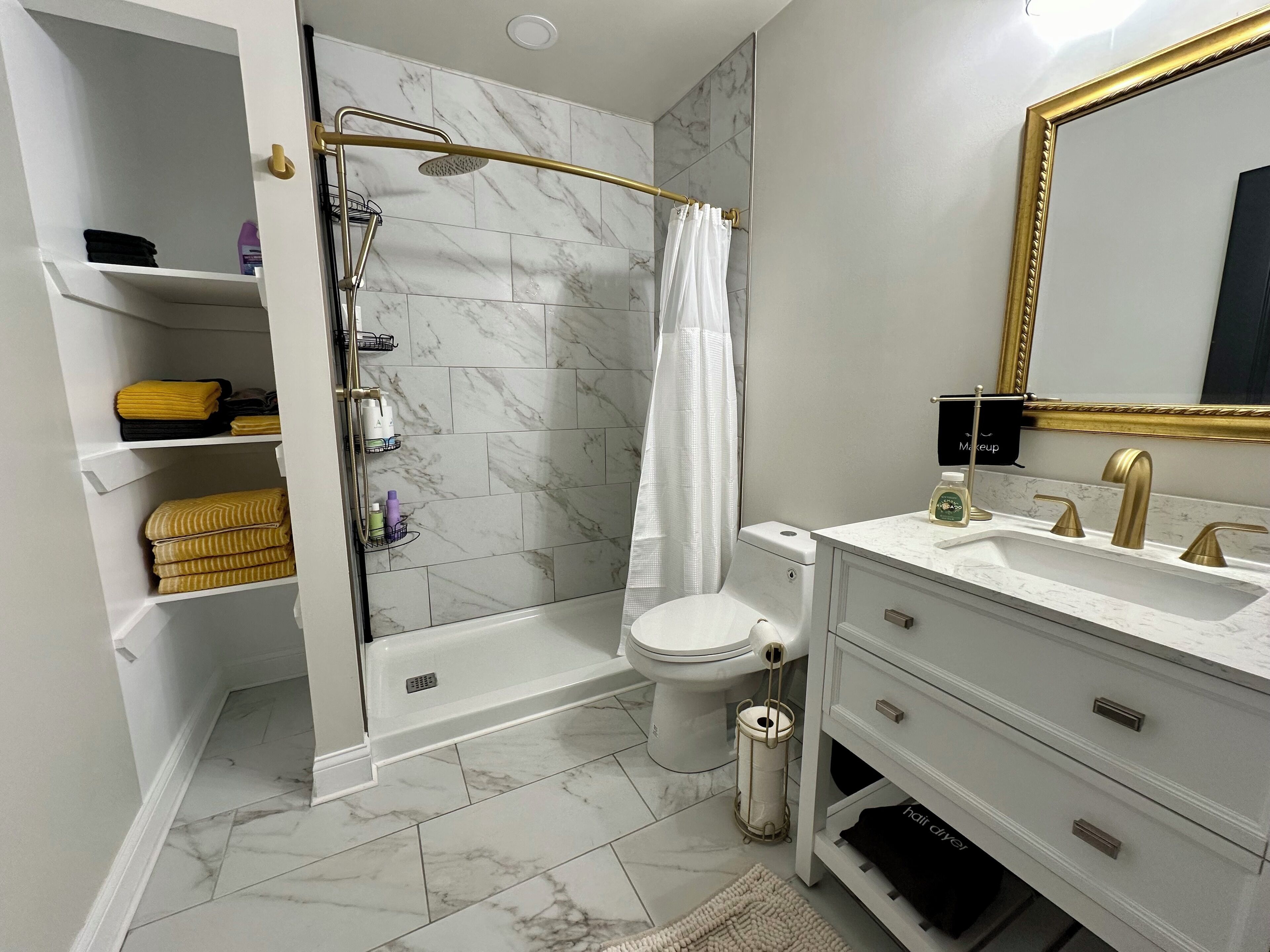A modern bathroom with a shower, toilet, vanity, and marble-tiled walls.