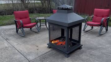 A patio area with a metal fire pit, two red chairs, and a table.