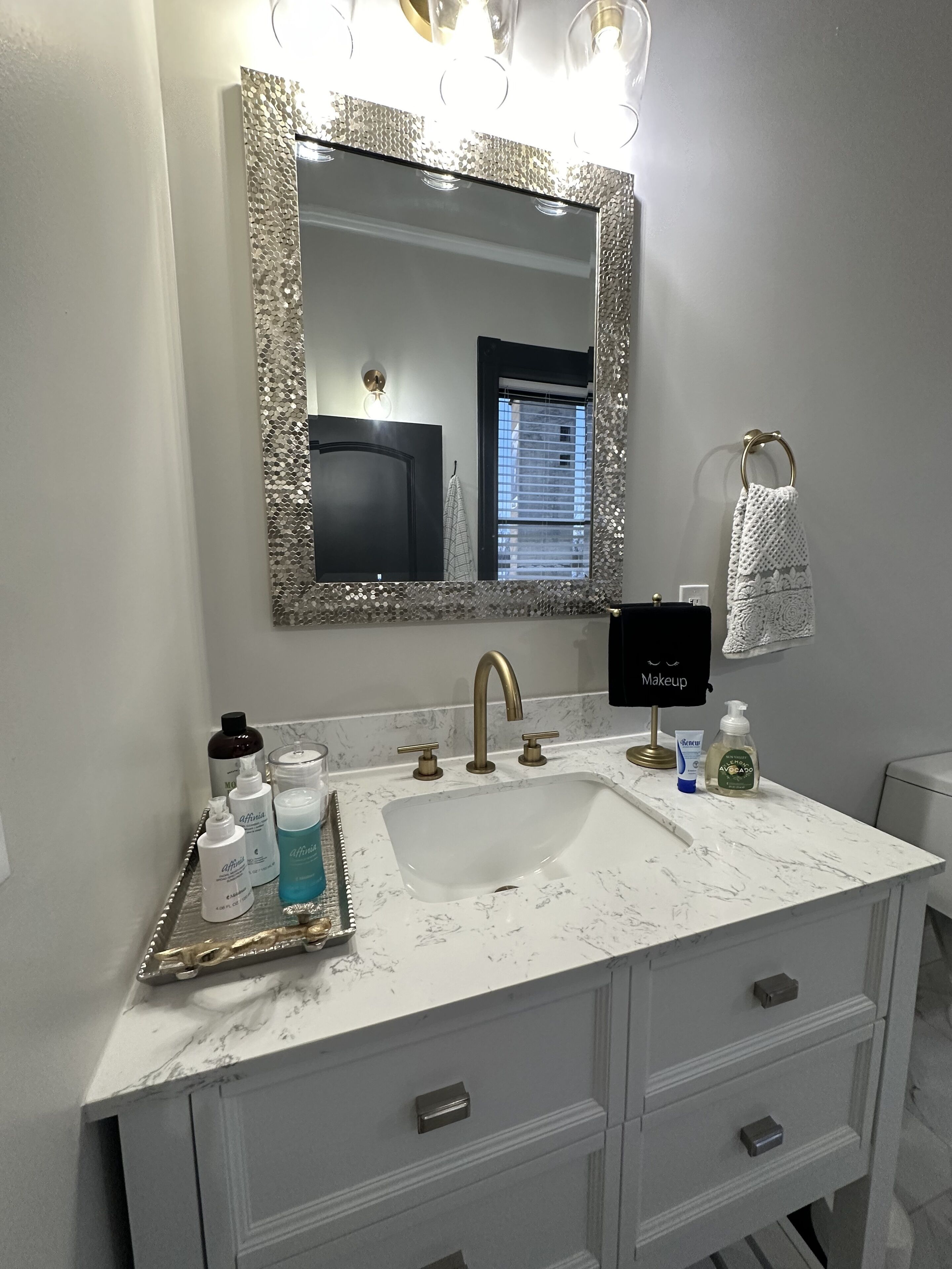A bathroom with a white marble sink, a large mirror with a decorative frame, and a vanity with drawers.