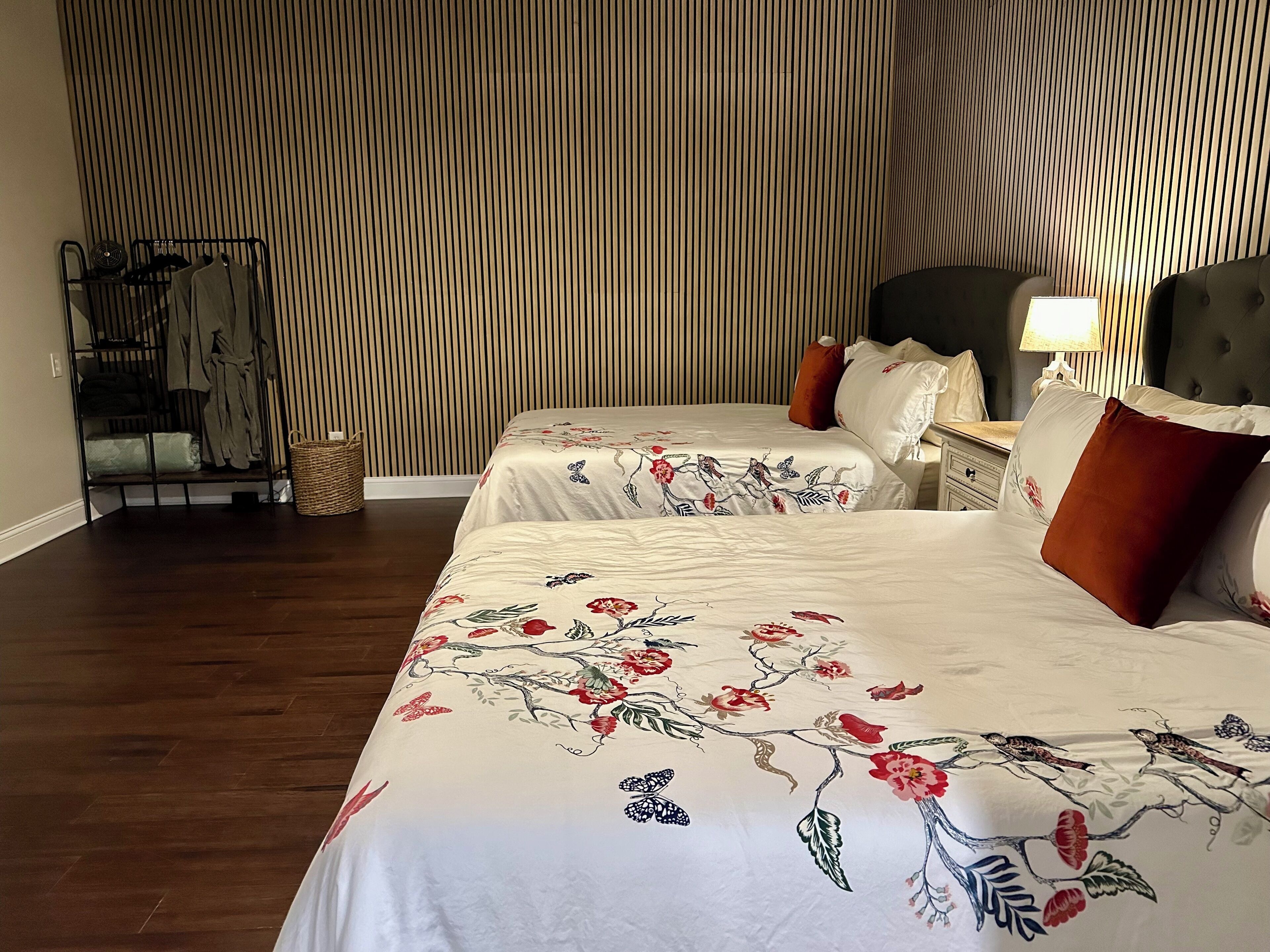 A hotel room with two beds, a wardrobe, a nightstand, and a lamp.