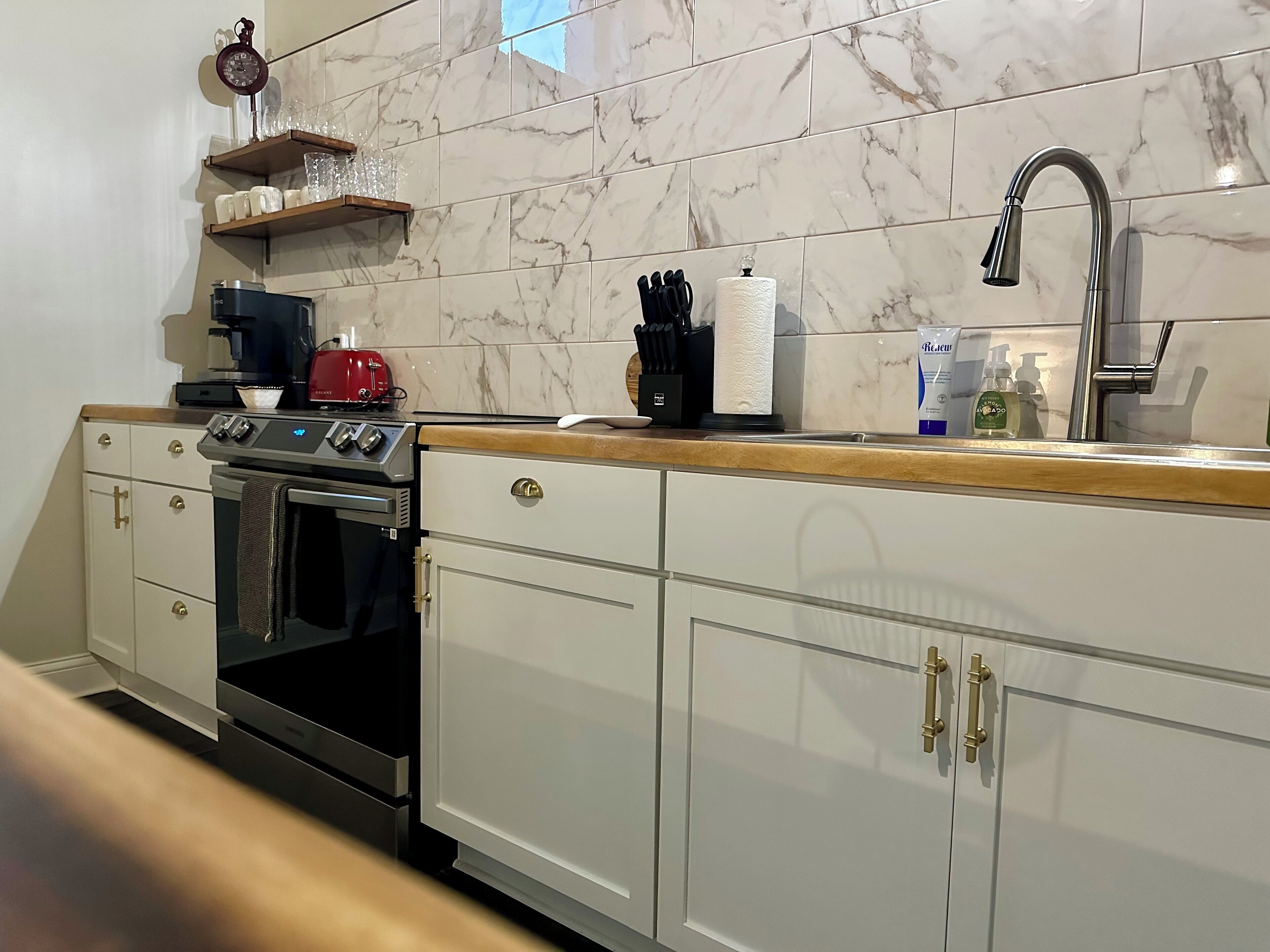 A kitchen with white cabinets, a stainless steel sink, and a marble backsplash.