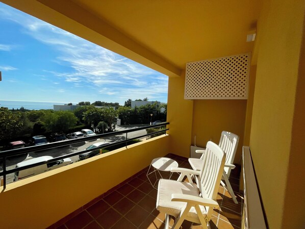 Un balcon avec des chaises blanches, une vue sur la mer et un mur jaune.