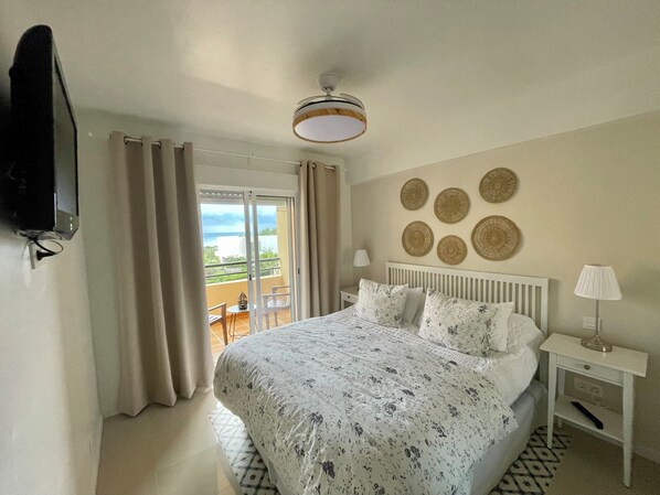 A bedroom with a bed, a nightstand, a lamp, and a view of the outdoors through a sliding door.