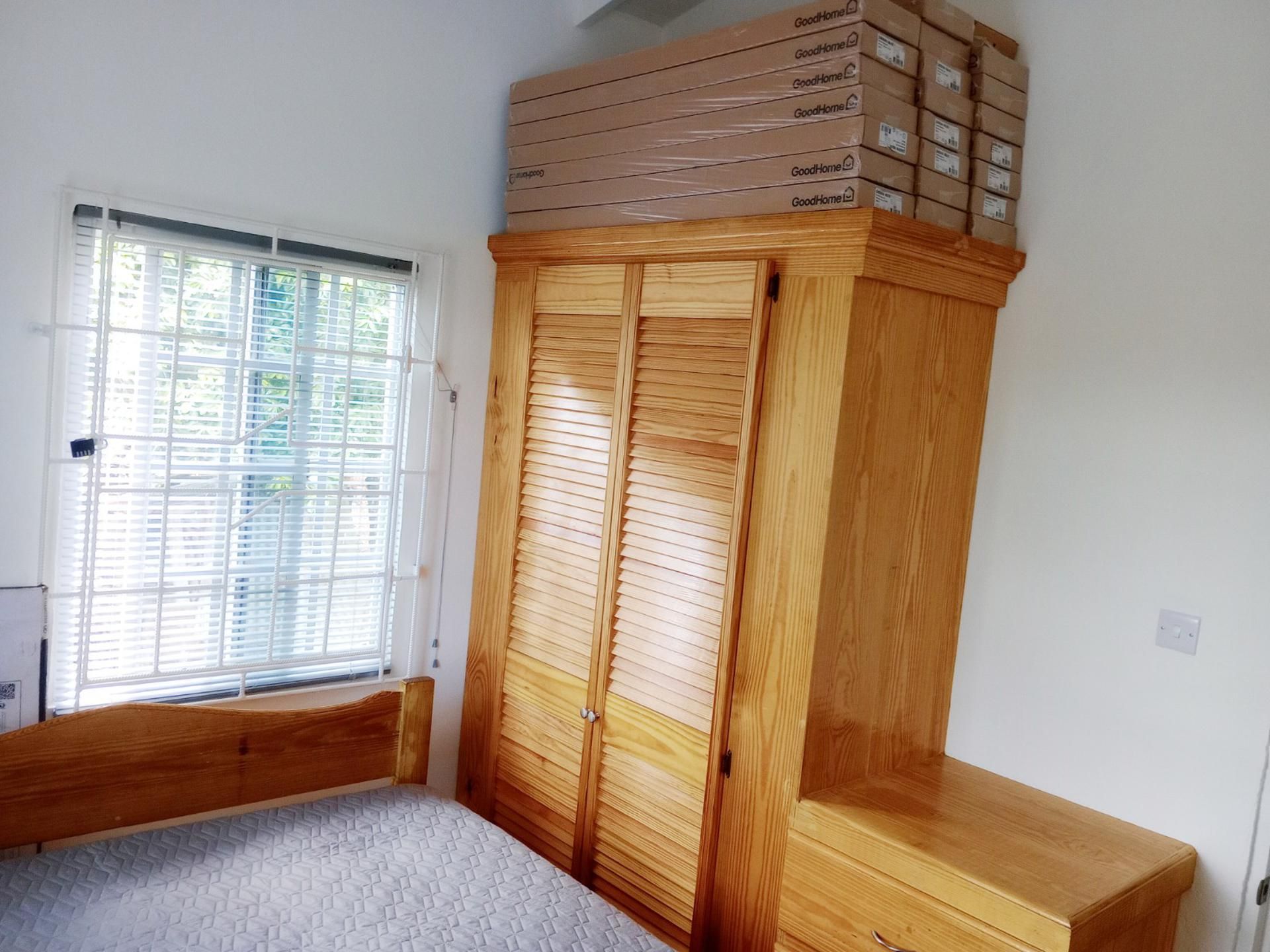 A bedroom with a wooden wardrobe, a window with blinds, and a bed.