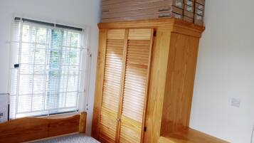 A bedroom with a wooden wardrobe, a window with blinds, and a bed.