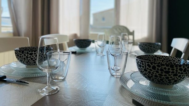 A dining table set with clear glassware and patterned bowls, with a view of the outdoors through large windows.