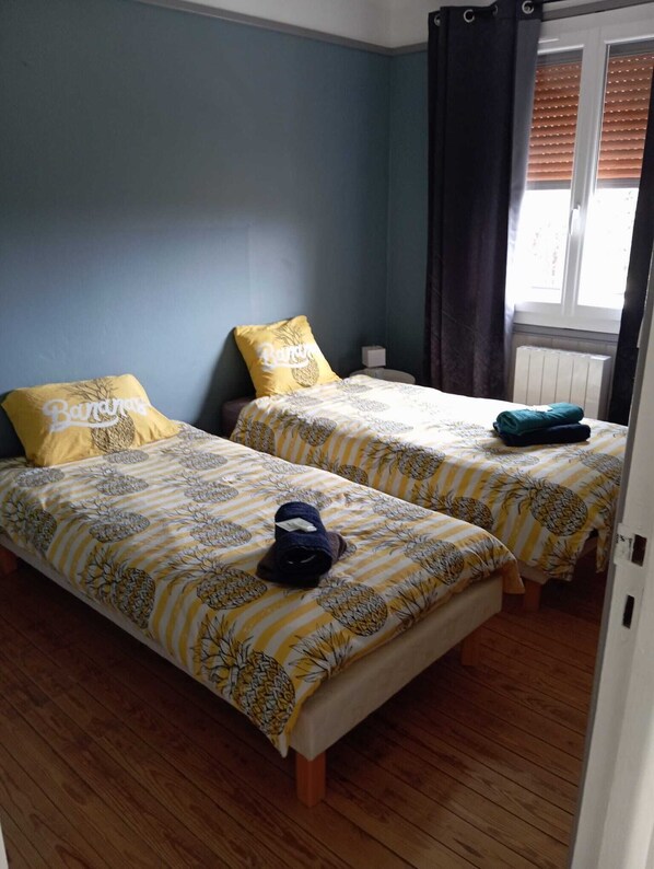 Una habitación con dos camas, cada una con una colcha de diseño de piña, una mesita de noche y una ventana con persianas.