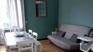 A living room with a dining table, chairs, a sofa, and a baby stroller.