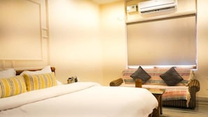 A hotel room with a large bed, a sofa, and a small table. There is an air conditioning unit on the wall. - A room facing the holy Ganges (Muni Ki Reti, Rishikesh)