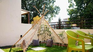 A grassy outdoor area with a teepee structure, a green plastic chair, and a white wall. - A room facing the holy Ganges (Muni Ki Reti, Rishikesh)