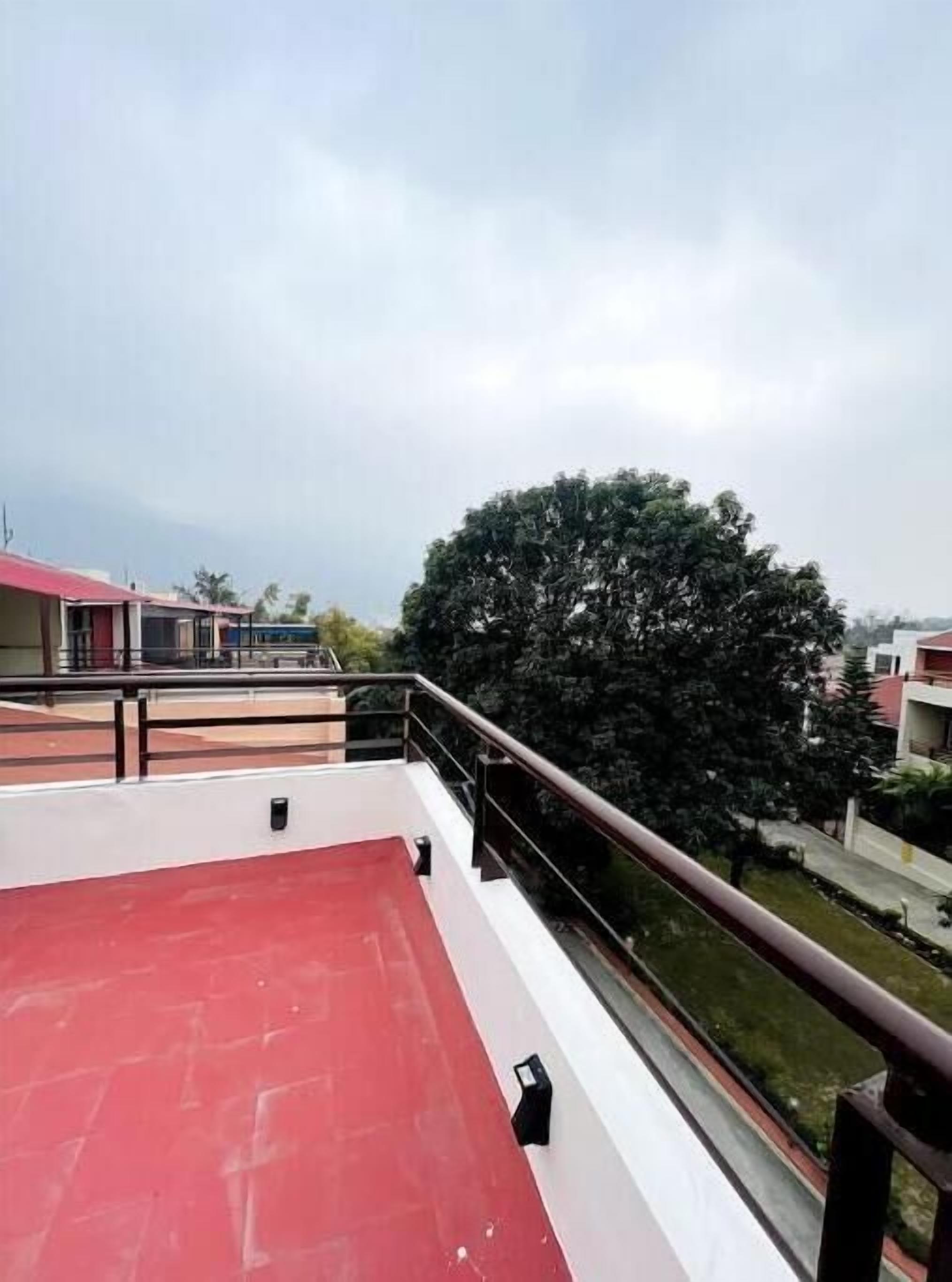 A red rooftop terrace with a railing, a small black object on the floor, and a view of surrounding buildings and trees.