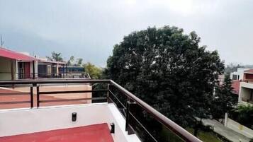 A red rooftop terrace with a railing, a small black object on the floor, and a view of surrounding buildings and trees.