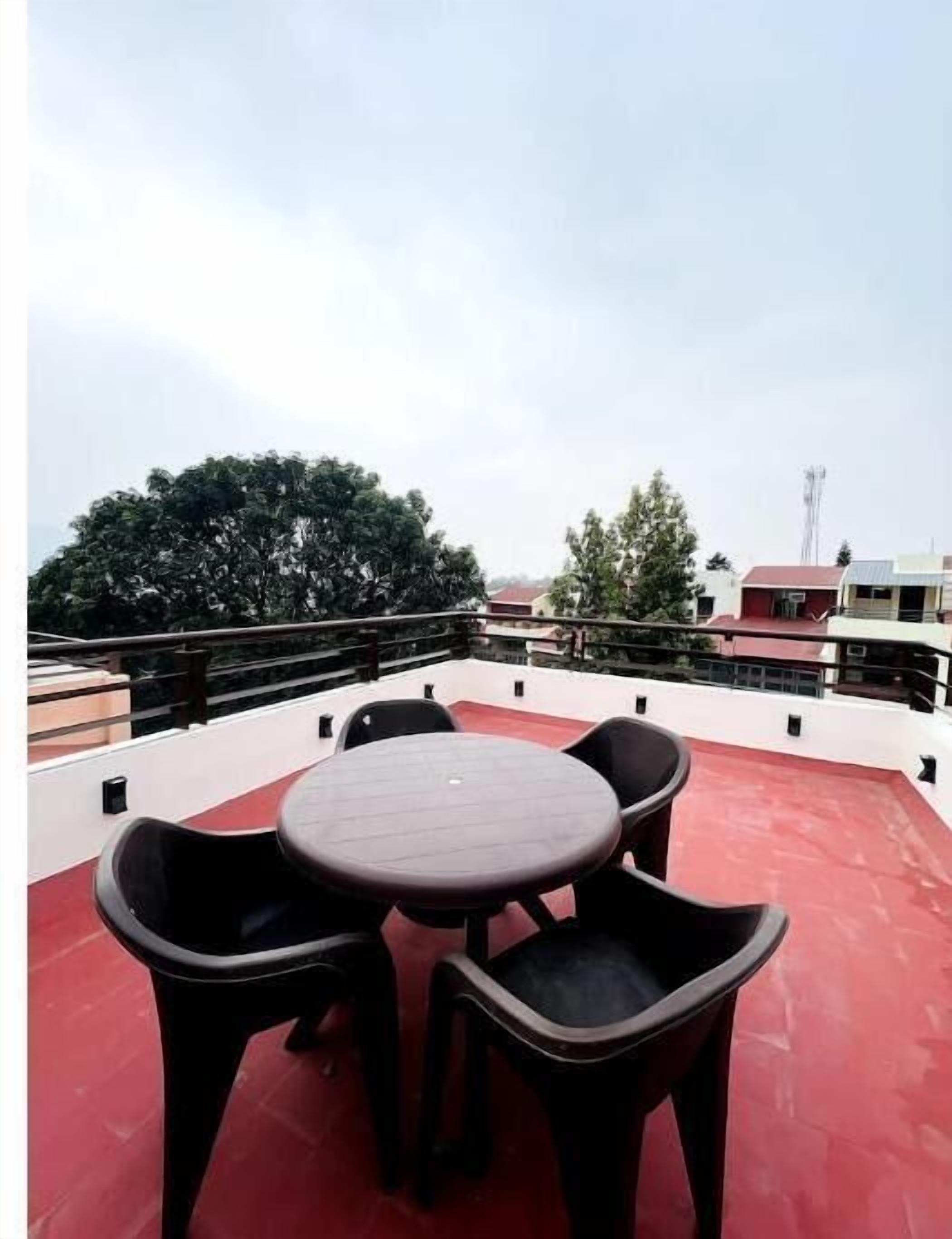 Une terrasse sur le toit, avec une table ronde et quatre chaises, entourée d’un sol rouge et d’une rambarde en métal.