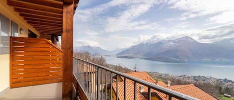 A balcony with a wooden floor and railing, overlooking a lake and mountains.