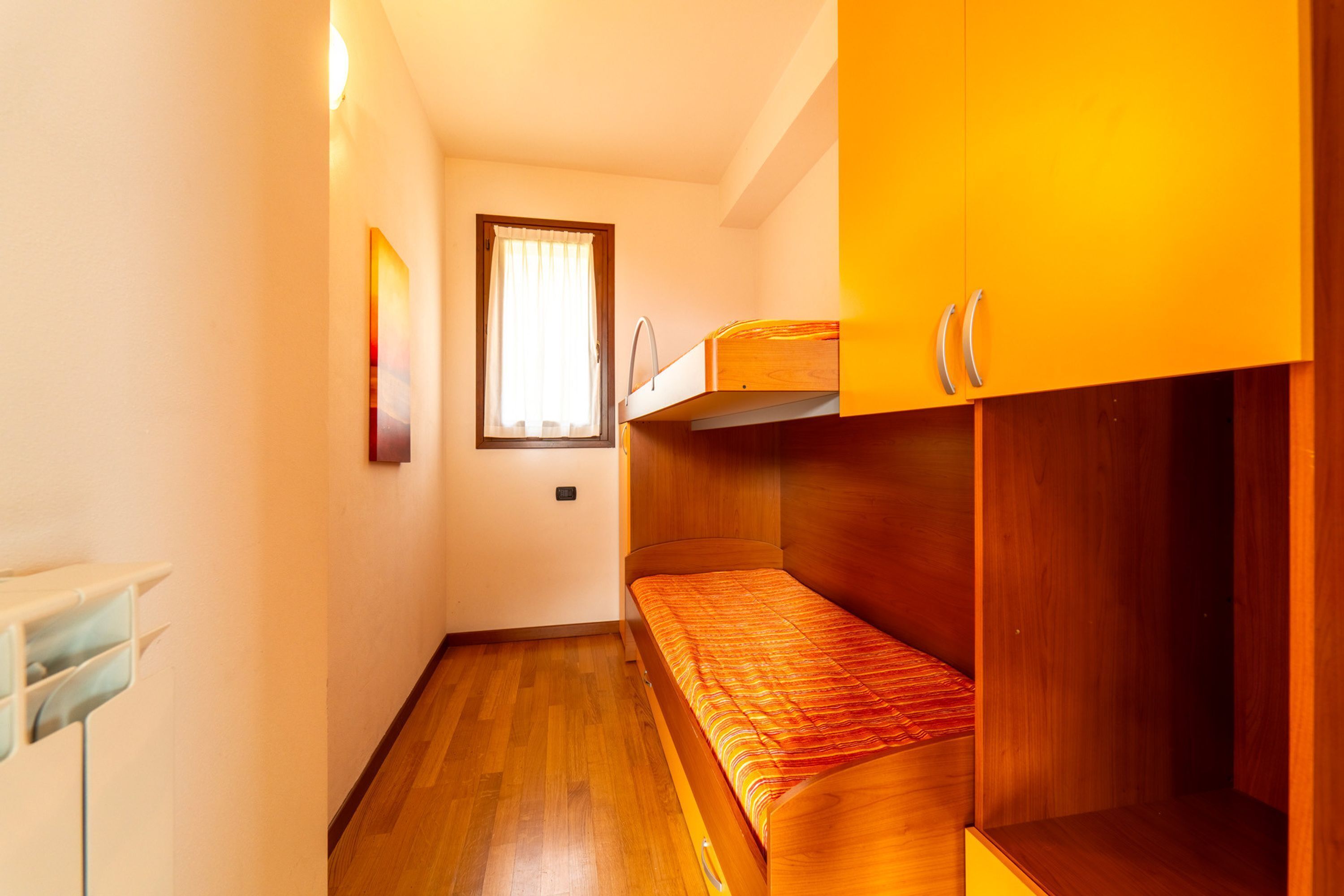 Quarto pequeno com cama de beliche, guarda-roupa de madeira e janela com cortinas.