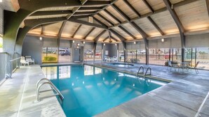 Una piscina techada con techo curvo, sillas de descanso y vista al estacionamiento.