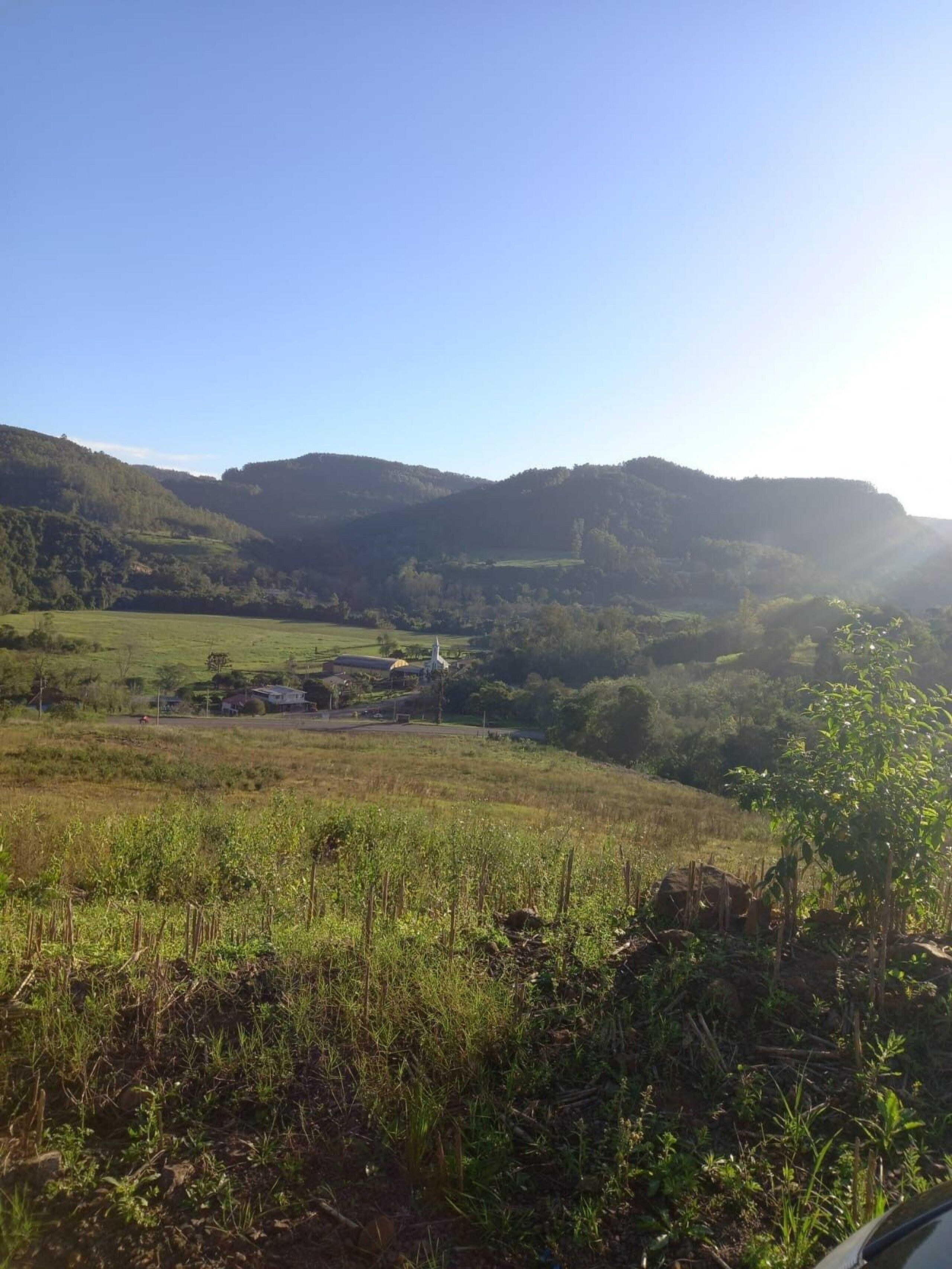 A rural landscape with rolling hills, a small building, and a clear sky.