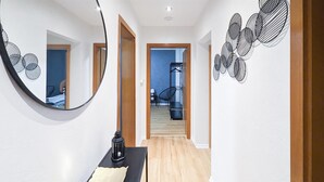 Ein Flur mit Holzboden, einem runden Spiegel und einem schwarzen Tisch mit einer Laterne. Im Hintergrund ist eine Wendeltreppe zu sehen.