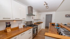 A modern kitchen with white cabinets, a wooden countertop, a gas stove, and a built-in oven. - Tarka Summerhouse - Four Bedroom House, Sleeps 8 (Woolacombe)