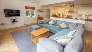 A modern living room with a grey sectional sofa, a wooden coffee table, and a TV mounted on the wall. - Tarka Summerhouse - Four Bedroom House, Sleeps 8 (Woolacombe)